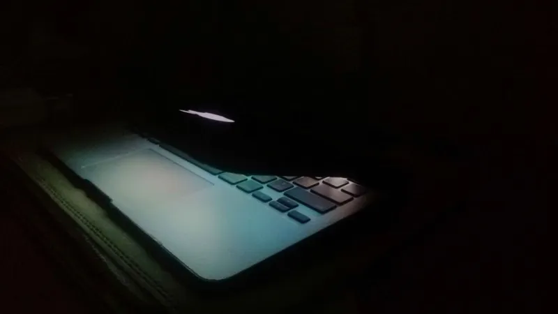 A laptop in a dark room with only the screen's light illuminating the surroundings.
