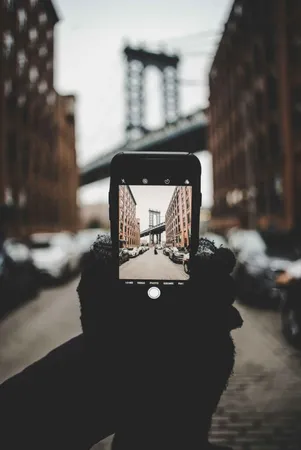A person holding a telephone and taking a photo of a bridge in the background. A person holding a telephone and taking a photo of a bridge in the background.