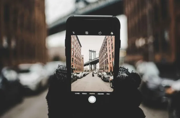 A person holding a telephone and taking a photo of a bridge in the background.