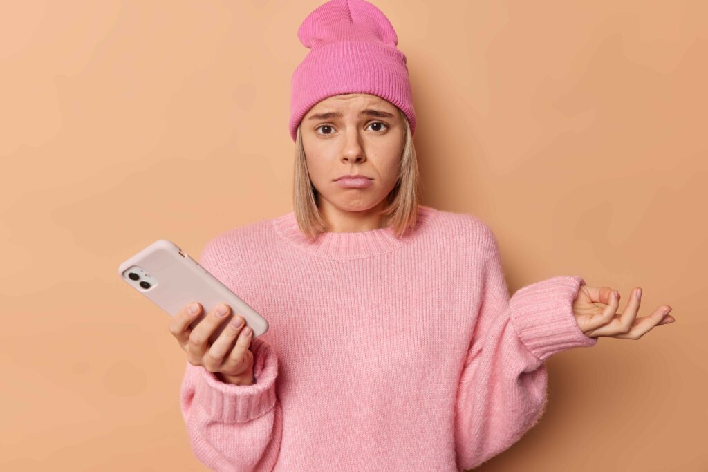 Upset girl looking at her phone, possibly reacting to being blocked on social media.