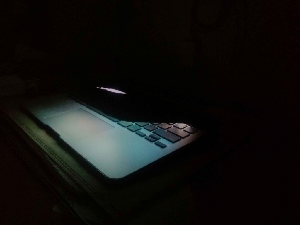 A laptop in a dark room with only the screen's light illuminating the surroundings.