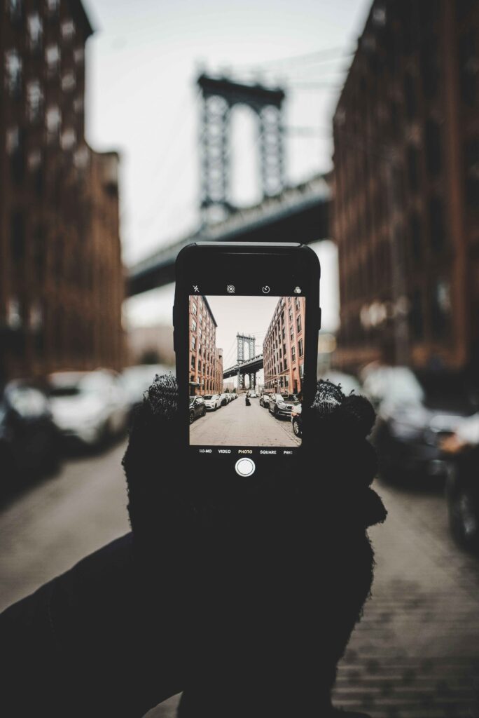 A person holding a telephone and taking a photo of a bridge in the background.